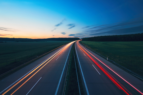 Landstraße mit Fahrtlichtern in der Dämmerung